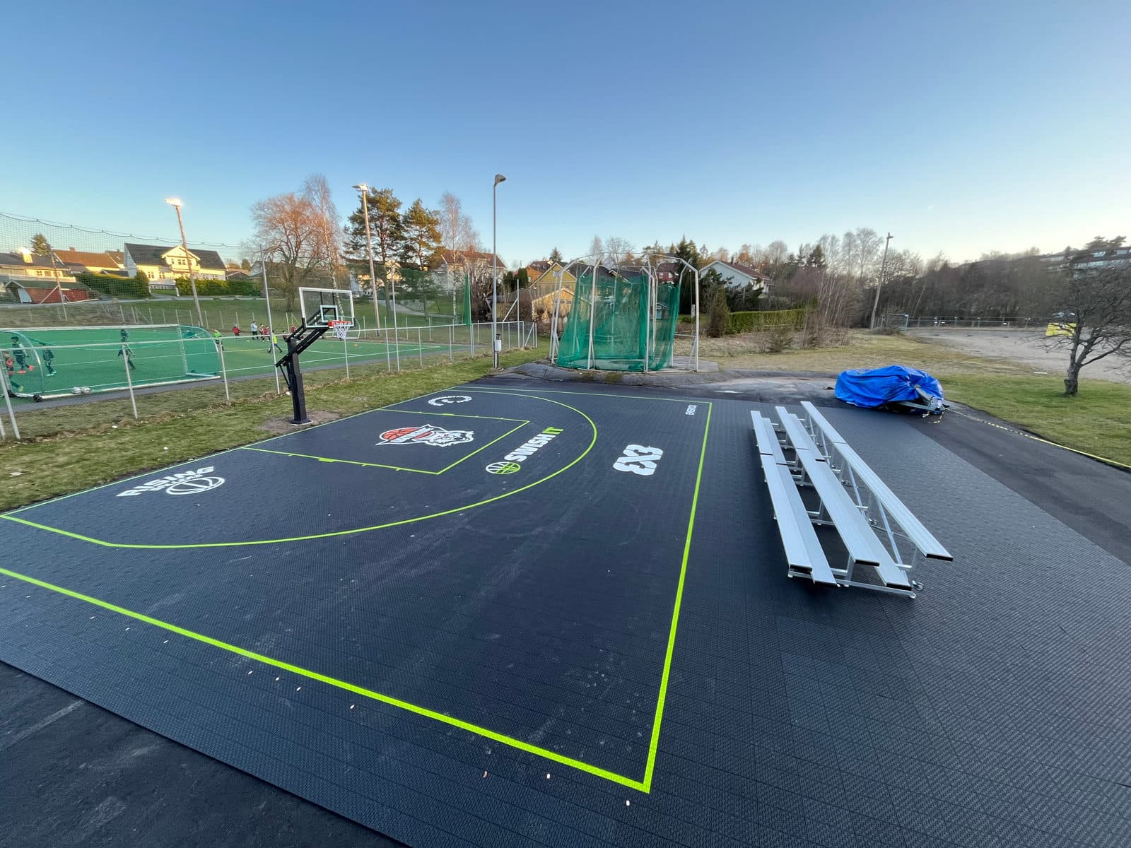 Nylagt 3x3-bane med svart dekke og grønne linjer, med tribuner under montering.